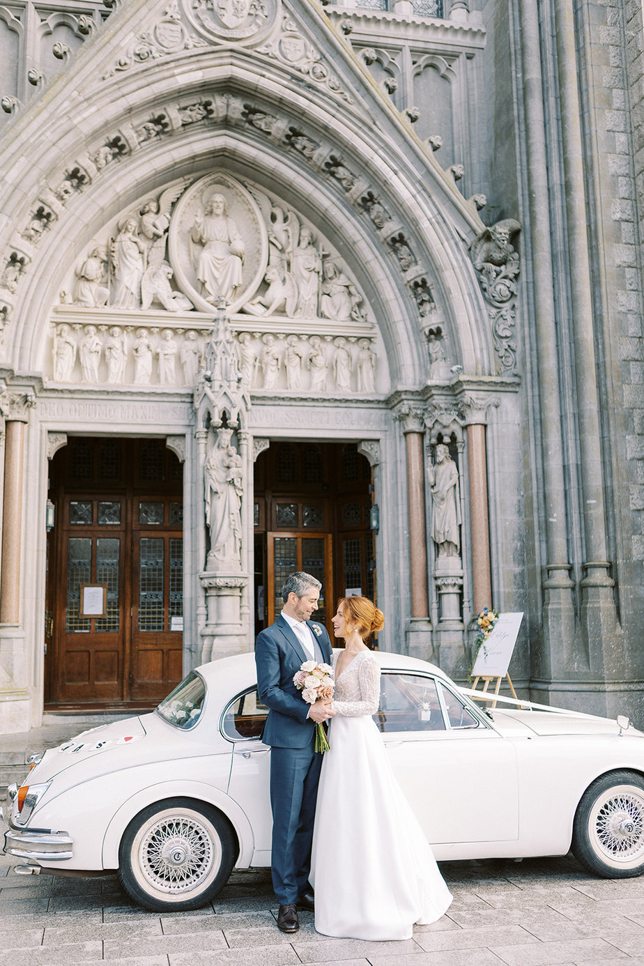 Bride and groom in front of white wedding car and in front of church cathedral