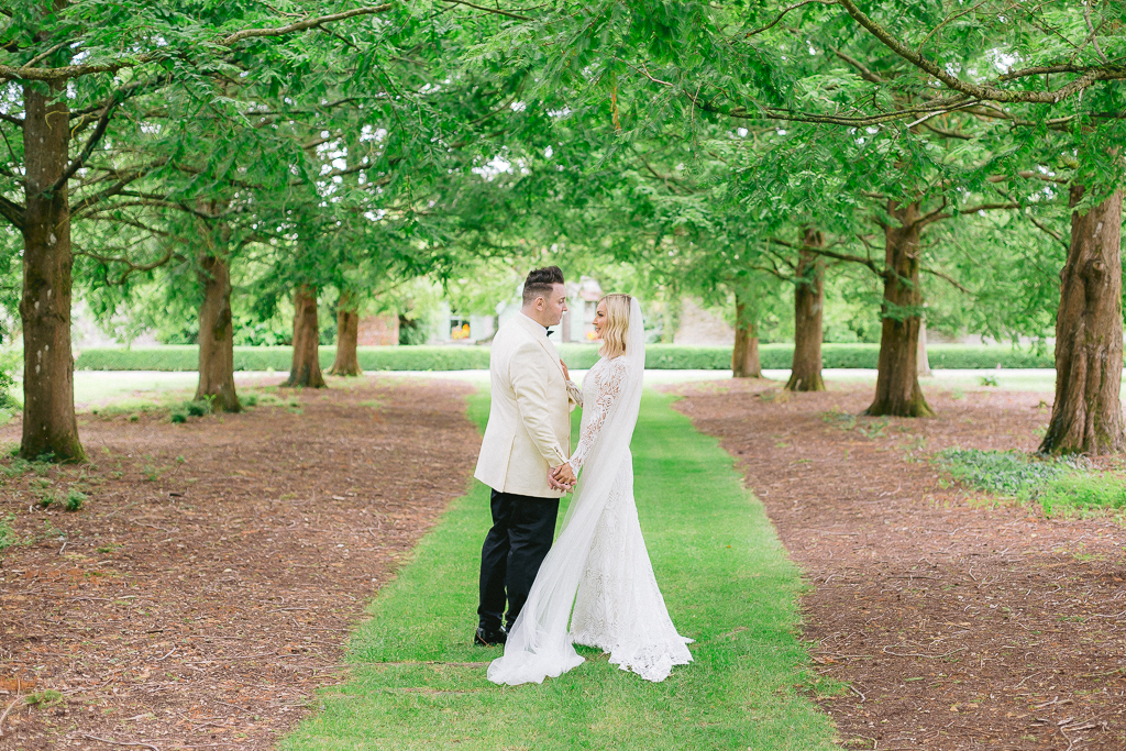 Bride and groom walk along patch of green grass in forest park